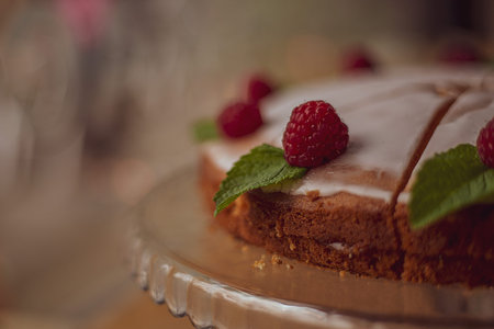 cake with white icing decorated with fresh raspberries and mint leaves on a wooden table in a cafe.