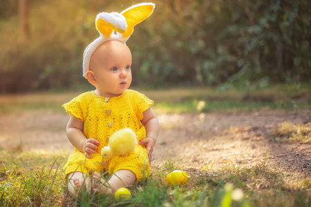 Cute little baby with bunny ears on Easter day. The girl hunts for Easter eggs on the lawn. Girl...