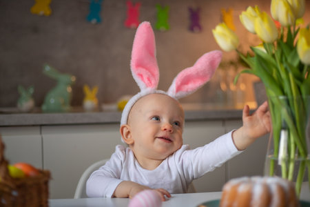 happy cute little baby girl wearing bunny ears on easter day sitting at the table in the kitchen.の写真素材