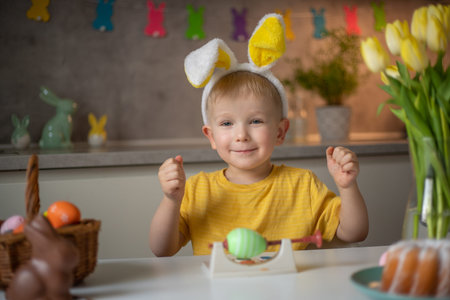 Emotional portrait of a cheerful little boy wearing bunny ears on Easter day who laughs merrily,...