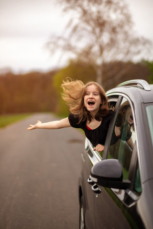 a happy girl with her hair fluttering in the wind looks out of the car window on a summer day.の写真素材