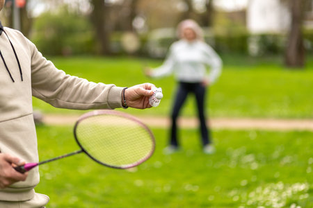 Man and woman playing badminton outdoors, focus on hand with shuttlecock.の写真素材