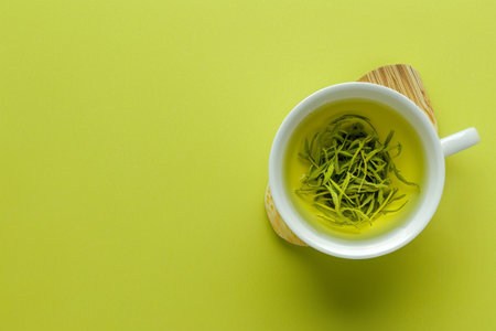 Cup of green tea on a bamboo stand with a green background.の素材