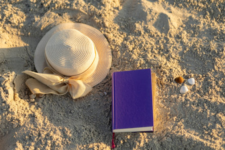 Relaxing on the beach with a hat, a book, and seashells during a sunny dayの写真素材