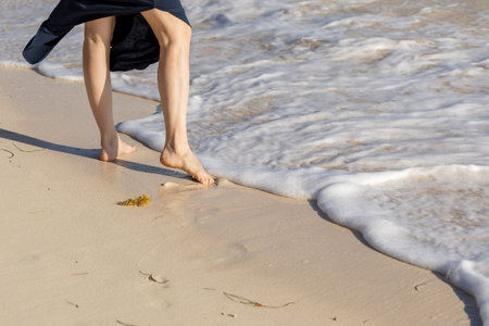 Walking barefoot along the shore while waves gently lap against the sand during a sunny day at the beachの写真素材