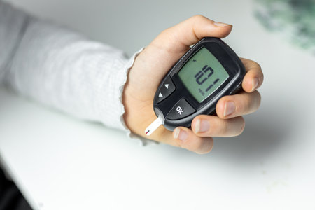 Hand holding a blood glucose monitor showing reading in a domestic setting during the dayの写真素材