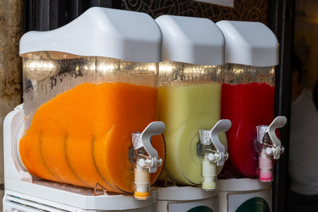 Colorful beverage dispensers filled with tropical flavors in a vibrant market setting during the afternoonの写真素材