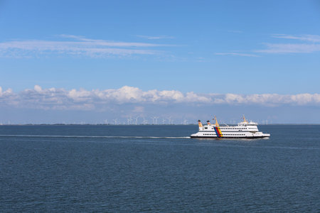 Ferry cruising across calm waters with wind turbines in the background on a clear day