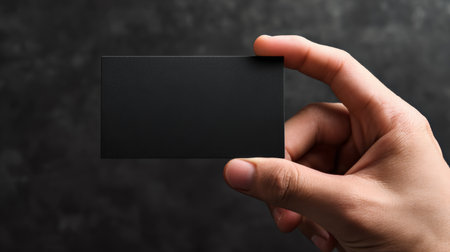 Person holding a blank black business card in a dark setting with a focus on the cards minimalistic design and textureの素材