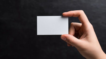 Hand holding a blank card against a dark background in a creative presentation settingの素材