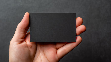 Unique black business card held in a hand against a dark textured background for branding ideasの素材