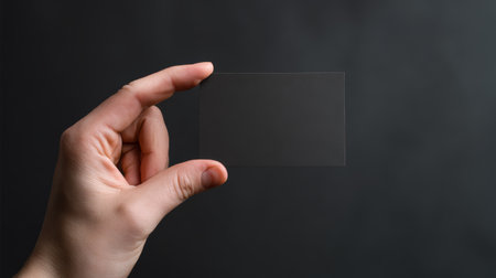 Transparent card held up against a dark background, showcasing its thin and minimalist design in a simple settingの素材