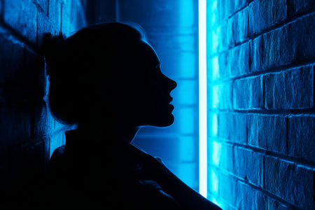 Silhouette of a woman in a narrow alley illuminated by soft blue light at nightの素材