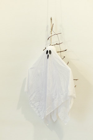 White ghost decoration hanging from a branch for a spooky Halloween atmosphereの写真素材
