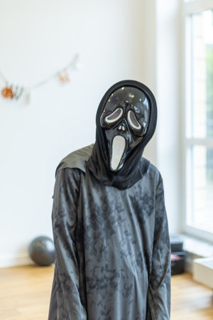 Scary figure in a dark costume with mask during a Halloween celebration in a bright indoor settingの写真素材
