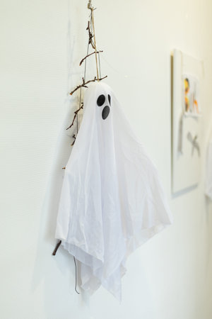 Creative ghost decoration made of white fabric and twigs hanging on a wall for Halloween celebrationの写真素材
