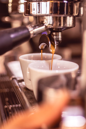 Fresh espresso brews from an espresso machine into elegant white cups in a cozy cafe settingの写真素材