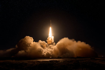 Rocket launch lights up the night sky with vibrant flames and thick smoke trailの素材