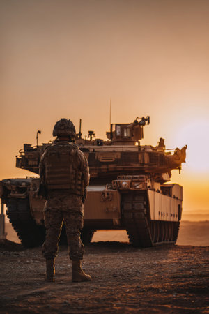 Soldier stands near tank during sunset in military training areaの素材