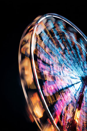 Colorful lights spin around the Ferris wheel at the fairground during the evening hours, creating a joyful atmosphere for visitorsの素材