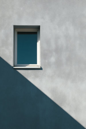 Window on a textured wall casting a long shadow in bright sunlight during a clear dayの素材