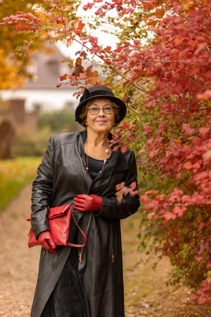 Stylish woman enjoying a walk in a colorful autumn park while wearing a leather coat and glovesの写真素材