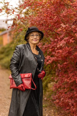 Stylish woman enjoying a fall day in a park with vibrant red foliageの写真素材