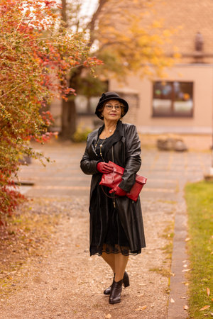 Elegant woman in black dress and hat strolls through autumn park with colorful leavesの写真素材