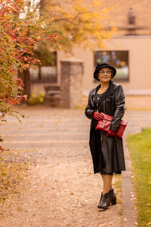 Stylish woman enjoying an autumn stroll in a park wearing a black dress and hat with red accessoriesの写真素材
