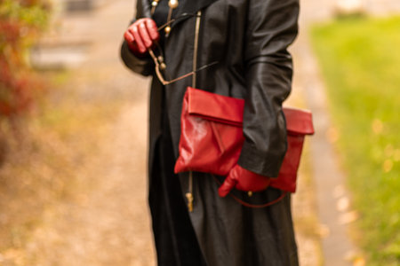 Stylish woman in black coat with red gloves and bag walking in a scenic park during autumnの写真素材