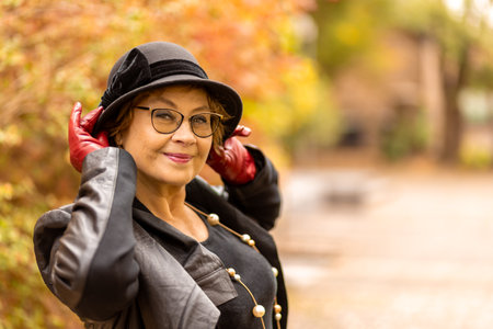 Confident woman poses in stylish attire with red gloves and hat during autumn walk in a park settingの写真素材
