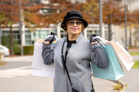 Woman enjoys shopping day in autumn with colorful bags in a city parkの写真素材