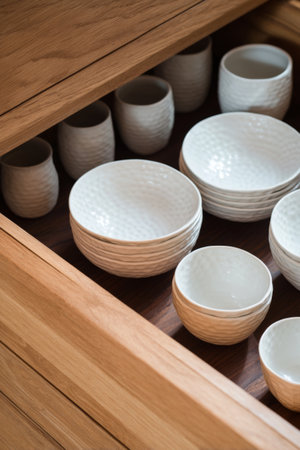 Beautifully organized wooden drawer featuring assorted white dishware in a cozy kitchen settingの素材