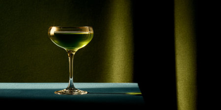 Elegant green cocktail sits on a table with dramatic lighting and shadows in a sophisticated settingの素材