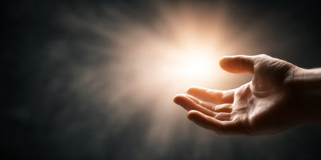 Hand reaching toward glowing light in dark studio symbolizes ambition and progressの素材