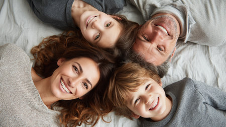 Happy family of four enjoying time together on a soft, light fabric surface under natural lightの素材