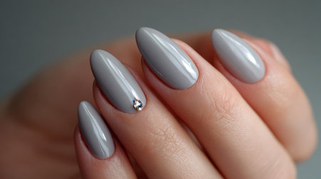 Elegant gray nail design featuring a decorative gem accent under soft lightingの素材