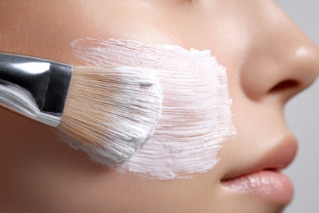 Woman applying facial mask with brush in skincare routine at home in bright, calming environmentの素材
