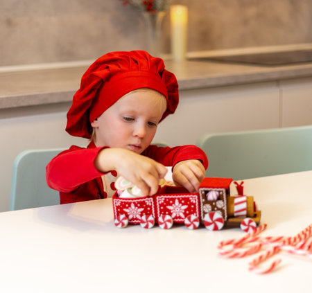 Child builds a colorful gingerbread train during holiday preparations at home in winterの写真素材