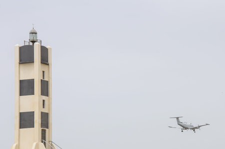 A lighthouse and Small private jet landing or taking off with background of grey sky