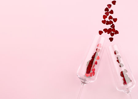 two wine glasses and confetti scattered in the form of hearts on a pink backgroundの写真素材