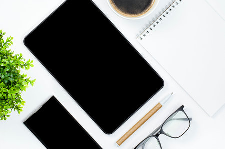 tablet computer, smartphone, notebook, coffee mug, flower, pen and eyeglasses on white table