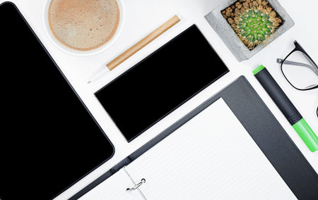 digital tablet, smartphone, coffee, cactus, glasses, notebook, pen and marker on a white desktop....