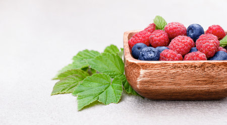 raspberries and blueberries in a wooden plate on a concrete background