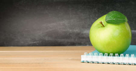 notebook and green apple on the table against the background of the chalkboardの写真素材