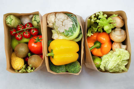 three paper bags with fresh vegetables and fruits on a light table, top viewの写真素材