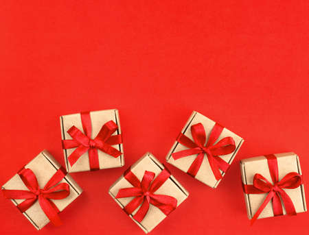 five small brown gifts with a red ribbon on a red backgroundの写真素材