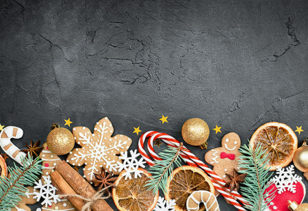 christmas composition of gingerbread, cinnamon, candy cane, orange, confetti and spruce twigs on a dark concrete backgroundの写真素材