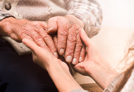 young female hands holding the hands of an elderly man