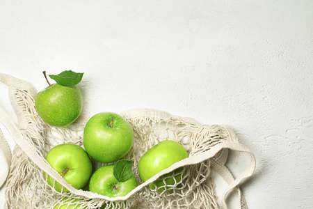 fresh green apples in a mesh bag on a light concrete table topの写真素材